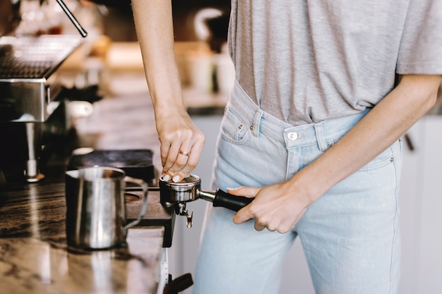 Une belle blonde mince aux cheveux longs, vêtue d'une tenue décontractée, prépare du café dans un café moderne. Le processus de préparation du café est montré. .