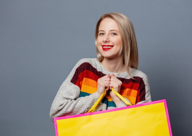 Belle blonde en pull avec des sacs à provisions sur gris