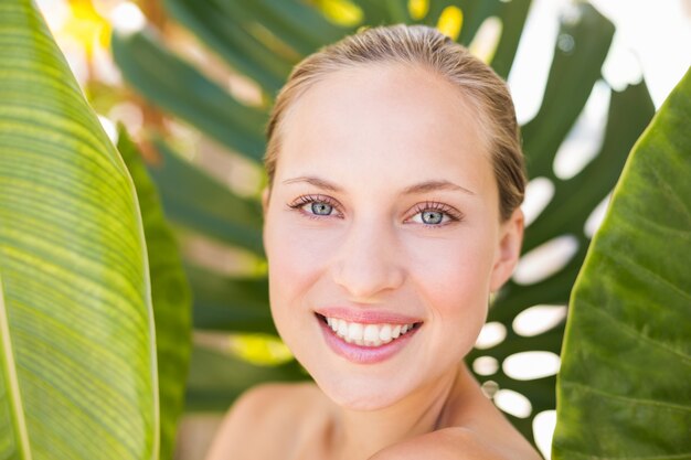 Belle blonde souriante à la caméra derrière la feuille