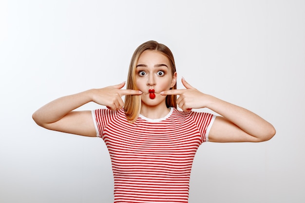 Une belle blonde en t-shirt blanc et rouge pose en studio sur fond blanc.