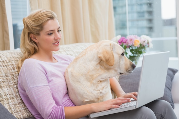 Belle blonde utilisant un ordinateur portable sur le canapé avec un chien