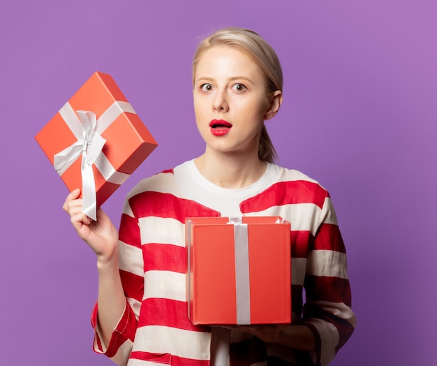 Belle blonde en veste rouge avec boîte-cadeau sur l'espace violet