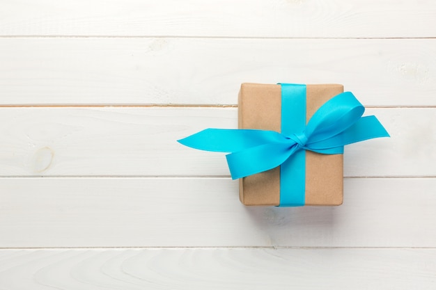Belle boîte-cadeau avec un arc bleu sur la table en bois blanche, vue de dessus