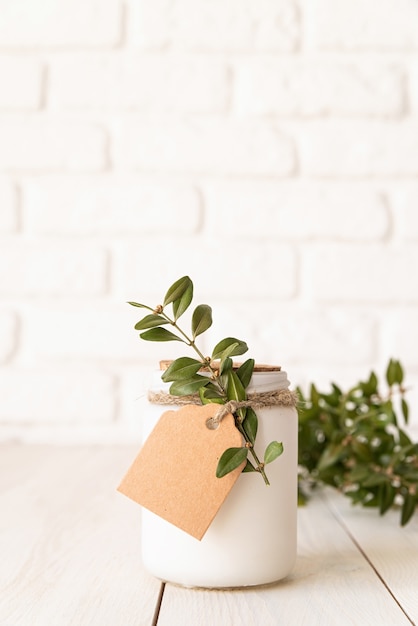 Belle bougie blanche avec des feuilles vertes fraîches sur une surface en bois blanche