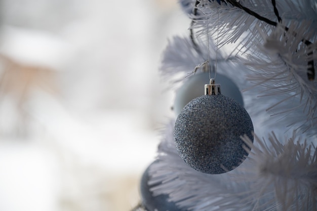 Belle boule de Noël bleu brillant suspendu à un arbre de Noël blanc avec une nature hivernale floue en arrière-plan.