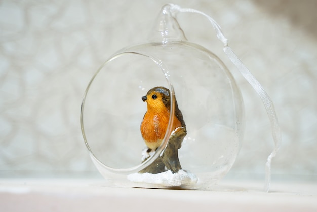 Belle boule transparente d'arbre de Noël avec un oiseau à l'intérieur se reposant sur une branche couverte de neige d'un arbre