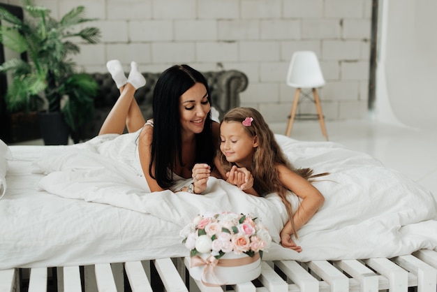 Belle et bronzée maman et fille sur un lit blanc avec des fleurs