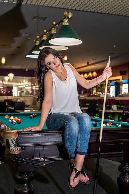 Belle brune assise sur une table de billard avec queue