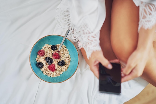 Belle brune au lit avec petit-déjeuner aux céréales avec téléphone