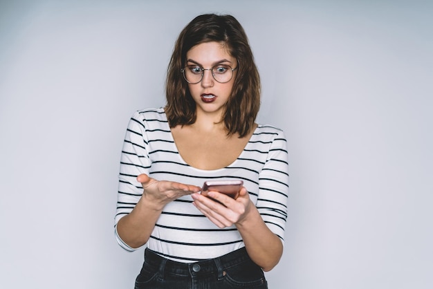 Belle brune au visage hébété pointant sur smartphone