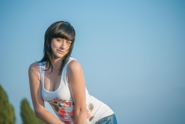 Une belle brune aux gros seins se dresse contre le ciel bleu dans un t-shirt blanc