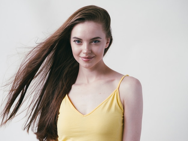 Belle brune aux longs cheveux lisses en chemise jaune portrait naturel sur fond blanc