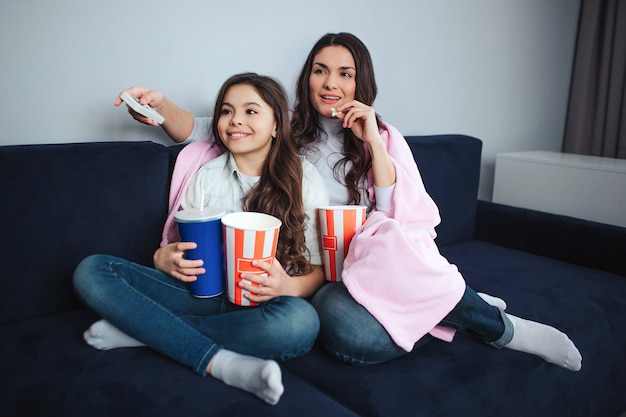 Belle brune caucasienne mère et fille s'asseoir ensemble dans la chambre. Ils regardent un film. Les gens tiennent des paniers à pop-corn et une tasse de cola. L'adulte a une télécommande. Calme et concentré.