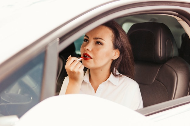 Belle brune élégante réussie jeune femme peignant ses lèvres avec rouge à lèvres en voiture