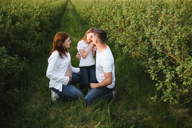 Belle brune enceinte maman et papa et fille en vêtements blancs se regardent dans la nature