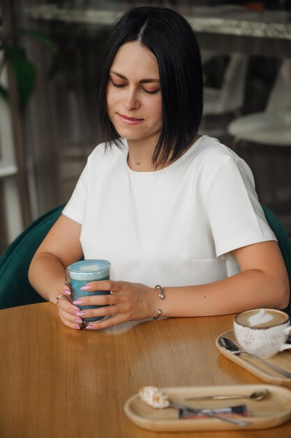 Belle brune est assise dans la salle à manger et boit du thé thaïlandais bleu avec du lait