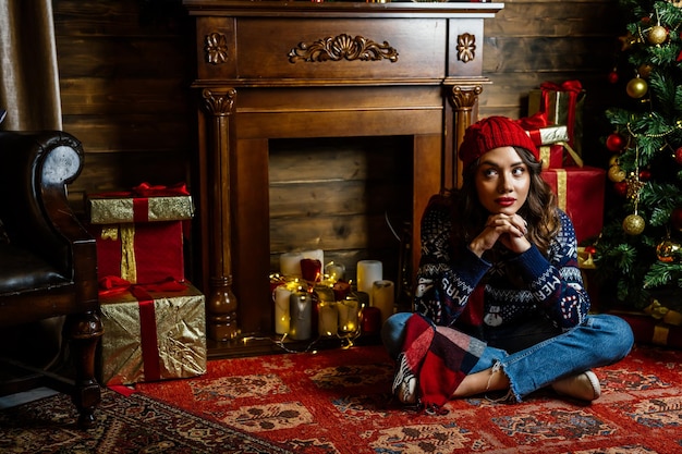 Une belle brune est assise sous un arbre de Noël sur fond de décorations du Nouvel An