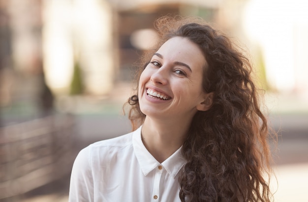 Belle brune femme bouclée, souriant à l'extérieur