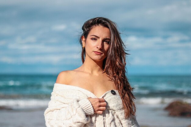 Belle et brune femme regardant la caméra sur la plage dans un pull