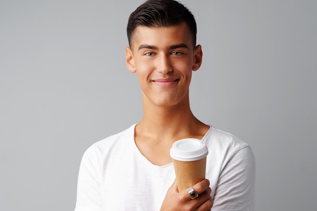 Belle brune jeune homme tenant une tasse de café sur un fond gris