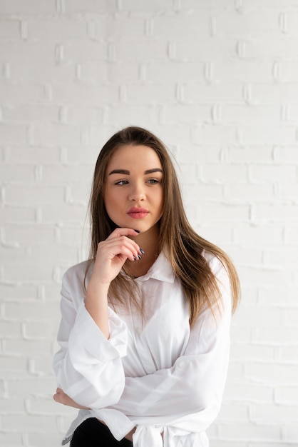 Belle brune maussade dans une chemise blanche sur fond blanc