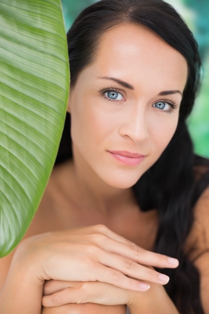 Photo belle brune nue, souriant à la caméra avec des feuilles vertes