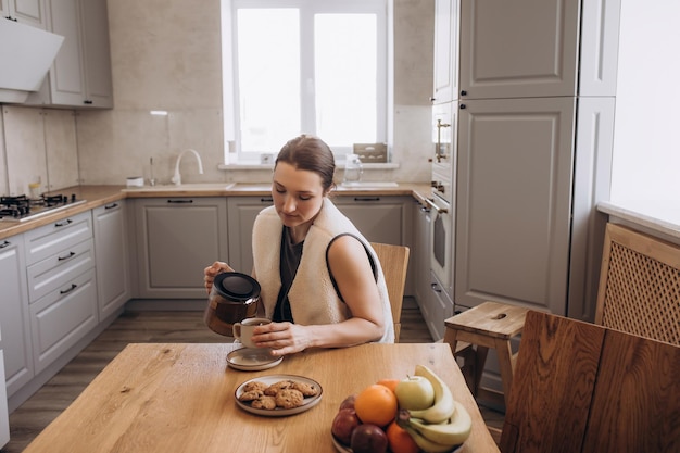 Une belle brune prend son petit déjeuner à la table de la cuisine avec une tasse de thé.