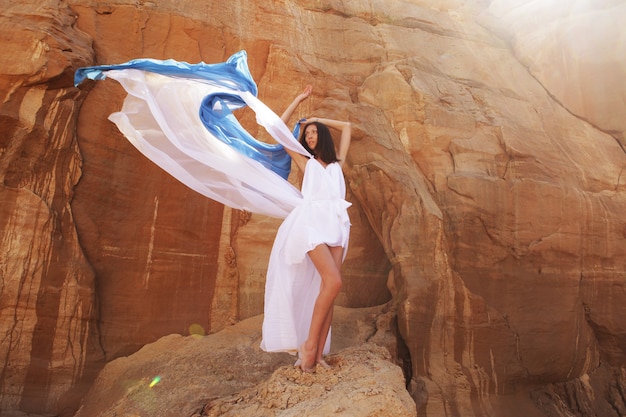 Belle brune en robe blanche avec tissu bleu dans le désert