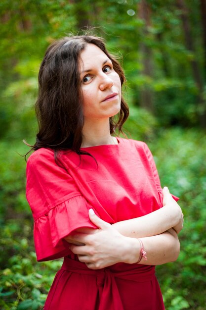 Belle brune en robe rouge marchant dans un parc ensoleillé