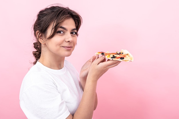 Belle brune en T-shirt blanc avec un morceau de pizza sur fond rose, copiez l'espace.