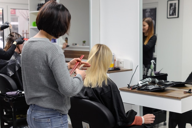 Belle brune travaillant comme coiffeuse coupe les extrémités des cheveux du client dans un salon de beauté