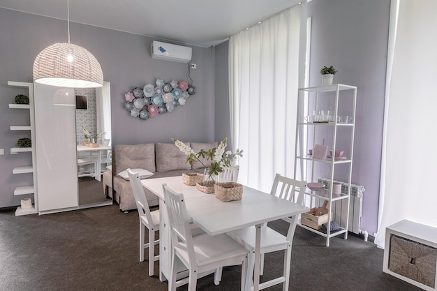 Belle chambre d'hôtel incroyable et lumineuse avec un intérieur et une décoration intéressants. Murs mats, table à manger blanche, moquette pleine grandeur, étagère blanche, armoire à miroir et canapé moelleux