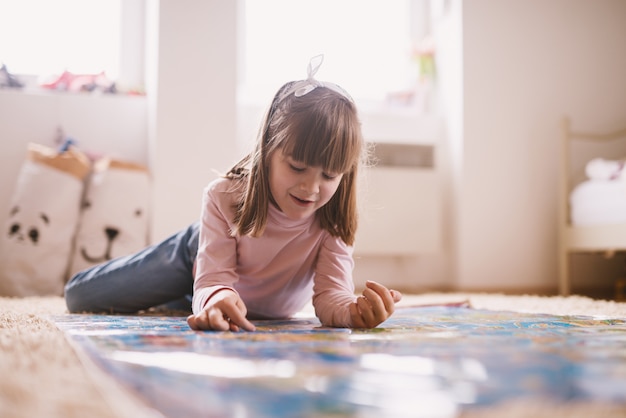 Belle charmante petite fille enfant en bas âge allongée sur le tapis de sa chambre et jouant avec une grande carte.