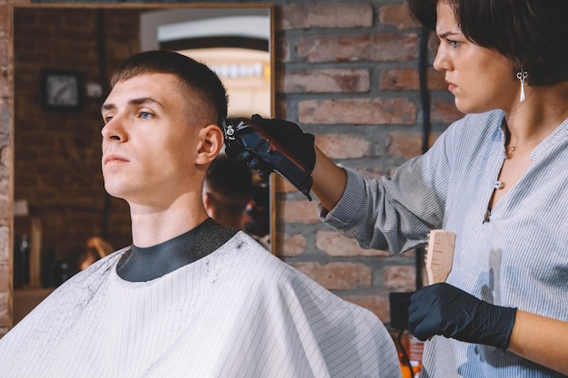 Une belle coiffeuse rase la tête du client avec une tondeuse électrique dans un salon de coiffure. Concept de publicité et de salon de coiffure