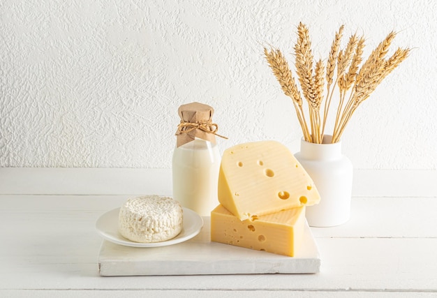 Belle composition festive pour la fête juive des produits laitiers Shavuot sur une planche de bois blanche et un vase avec des oreilles de pain fond blanc