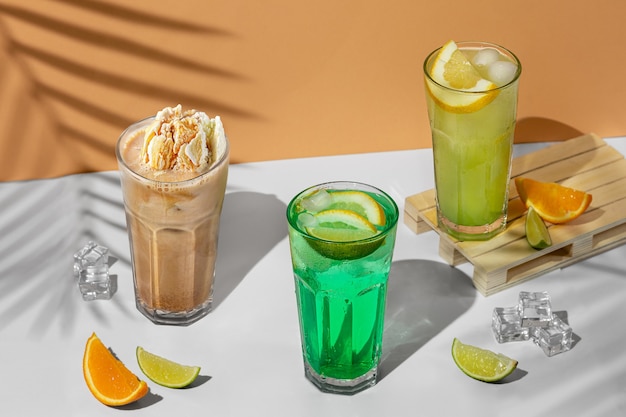 Belle composition de nature morte avec trois verres transparents de boisson d'été. limonade verte au citron vert, menthe, citron et agrumes sur fond tropical avec les ombres d'un palmier