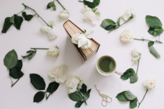 Belle composition romantique avec une tasse de thé vert matcha et des fleurs roses sur une surface blanche