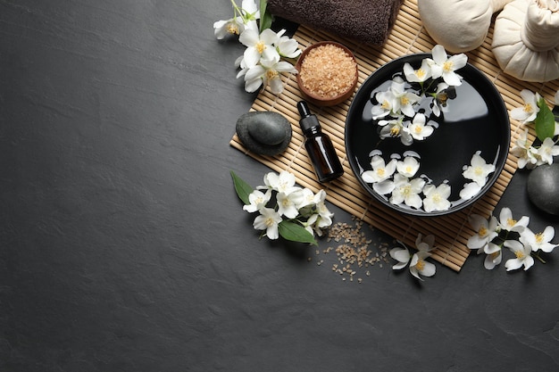 Belle composition de spa avec de l'huile essentielle de jasmin et des fleurs fraîches sur une table plate.