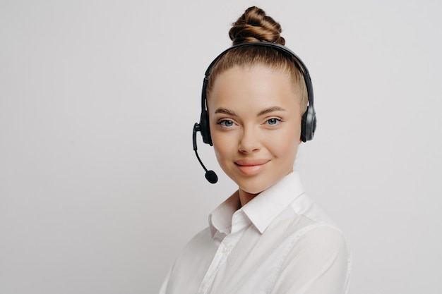 Une belle consultante en chemise blanche, casque noir, cheveux en crochet discute du fonds d'assurance du client en ligne, isolée près d'un mur lumineux.