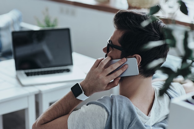 Belle conversation. Vue arrière du jeune homme en lunettes parler au téléphone intelligent et souriant