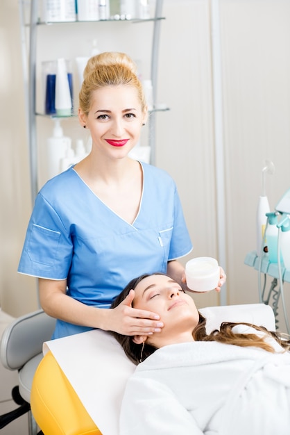 Belle cosmétologue en uniforme faisant un traitement facial au patient dans le bureau de cosmétologie