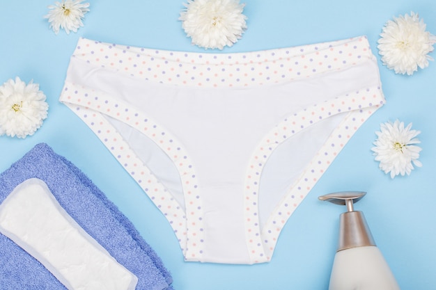 Belle culotte avec serviette, serviette hygiénique et bouteille de savon liquide sur fond bleu. Ensemble de sous-vêtements pour femmes. Vue de dessus.