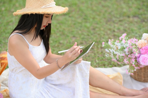 Belle dame à l'aide d'une tablette portable esquissant une vue de paysage lors d'un pique-nique dans le jardin