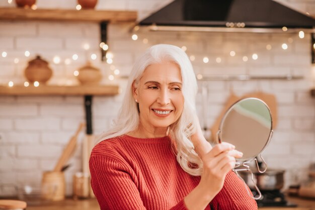 Belle dame aux cheveux gris en chemisier rouge en regardant le miroir