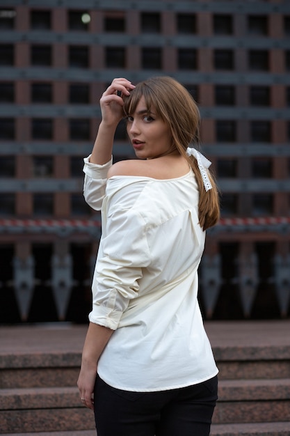 Belle dame brune porte une chemise blanche avec une épaule nue se promène dans la ville