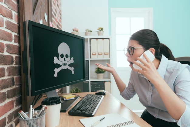 belle dame gestionnaire travaillant au bureau de l'entreprise lorsqu'elle ouvre un ordinateur trouvant un empoisonnement à l'aide d'un téléphone portable appelant à l'aide.