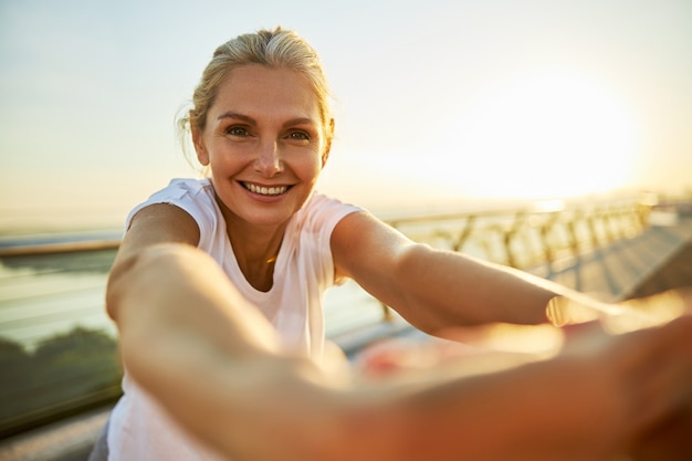 Belle dame regardant la caméra et souriant tout en faisant de la gymnastique matinale à l'extérieur