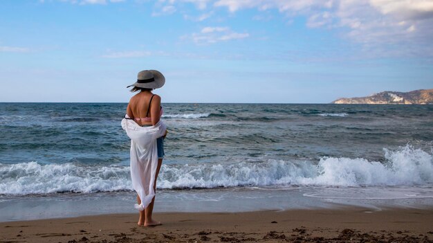 belle dame se tient sur une plage de sable et regarde au loin en admirant la mer déchaînée. Vue arrière