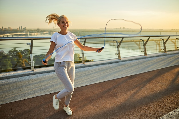 Belle dame souriante en tenue de sport faisant de l'exercice avec une corde à sauter sur le pont