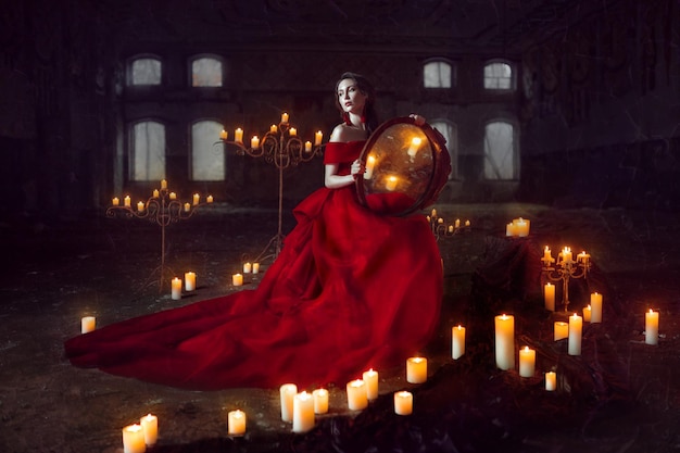 Belle dame vêtue d'une robe de bal rouge assise avec des bougies